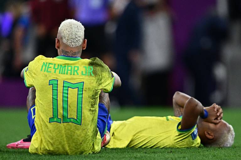 Neymar, de costas, usando a camisa 10, está sentado no gramado do estádio Cidade da Educação, em Al Rayyan. Ao seu lado, deitado e com as mãos no rosto, está Rodrygo. Os dois estão desolados depois da eliminação do Brasil diante da Croácia nas quartas de final da Copa do Qatar