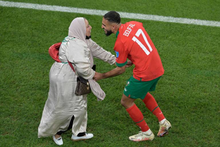 Jogador marroquino sorrindo e de mãos dadas com a mãe, que veste uma roupa cobrindo quase todo o corpo