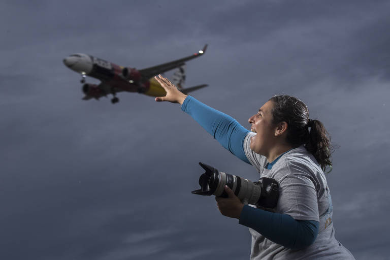 Gisele Orquídea, 40, acena para avião em praça que de Guarulhos que é usada para fotografar as aeronaves