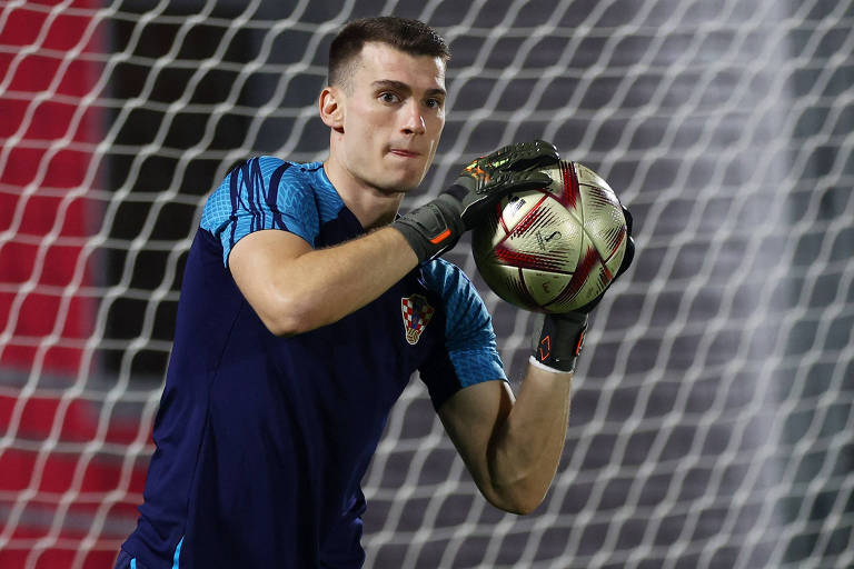 Imagem colorida mostra o goleiro Livakovic, do tórax para cima, segurando a bola com duas mãos, durante treino da seleção da Croácia
