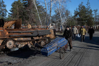 A man wheels a coffin down a street, tasked with reburying a child killed in the shelling whose death was being investigated by police in Sviatohirsk, Ukraine, Nov. 29, 2022. (Tyler Hicks/The New York Times)