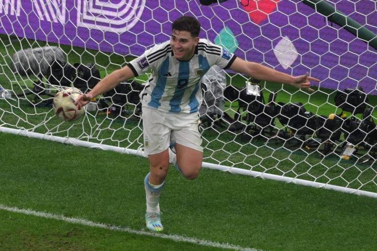 Imagem colorida mostra o jogador argentino Julián Álvarez, de 22 anos, de corpo inteiro. Ele está correndo com os braços abertos. Julián veste o uniforme da Argentina, com camisa branca e listra azul, calção e meião brancos.