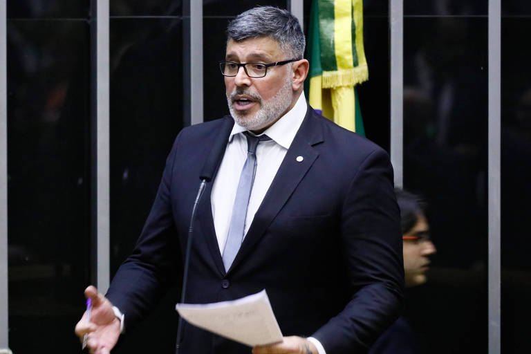 Em foto colorida, homem de terno escuro discursa em um parlamento