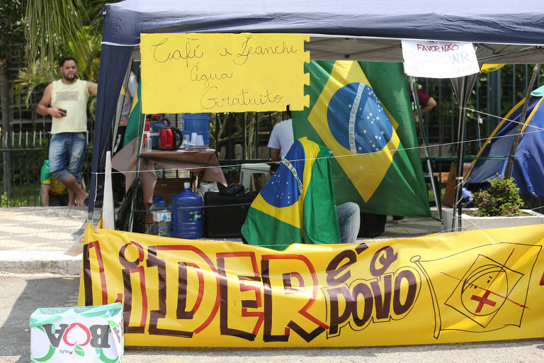 Barraca com cartaz amarelo no alto e faixa abaixo onde se lê "Líder é o povo" e se vê uma bandeira do Brasil desenhada (o contorno apenas) com uma carinha com um X na boca, como um símbolo de censura