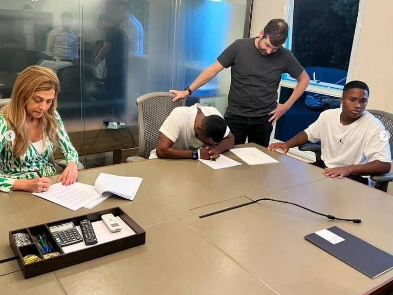 Presidente do Palmeiras, Leila Pereira assina o contrato de venda do atacante Endrick (à dir.) com o Real Madrid; de cabeça baixa na mesa, o pai do atacante, Douglas, chora de emoção
