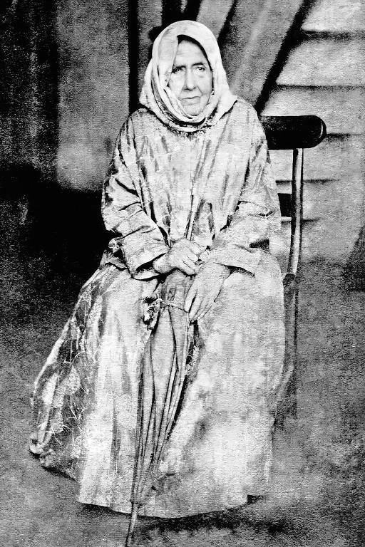 A foto mostra a beata Nhá Chica, sentada, com vestes longas de religiosa, e segurando um guarda-chuva.