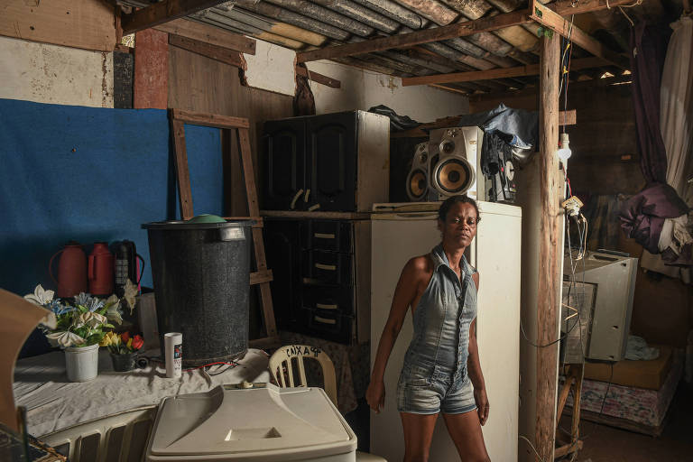 Mulher posa na frene de geladeira e outros móveis de seu barraco