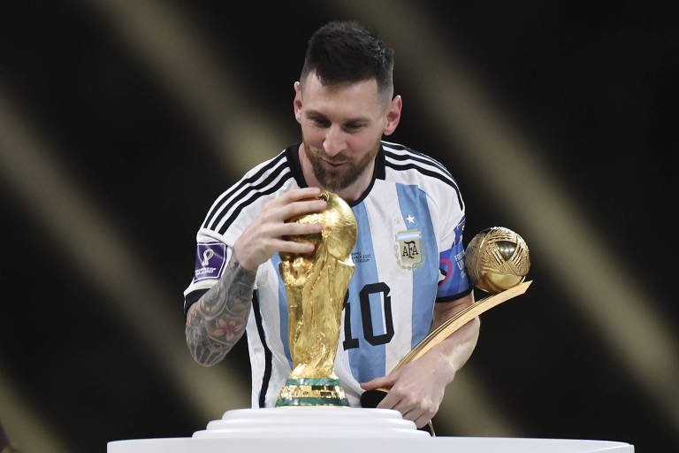 Com a camisa 10 da seleção argentina, Messi admira e toca na Taça Fifa no estádio Lusail, no Qatar, depois da vitória sobre a  França na Copa do Mundo