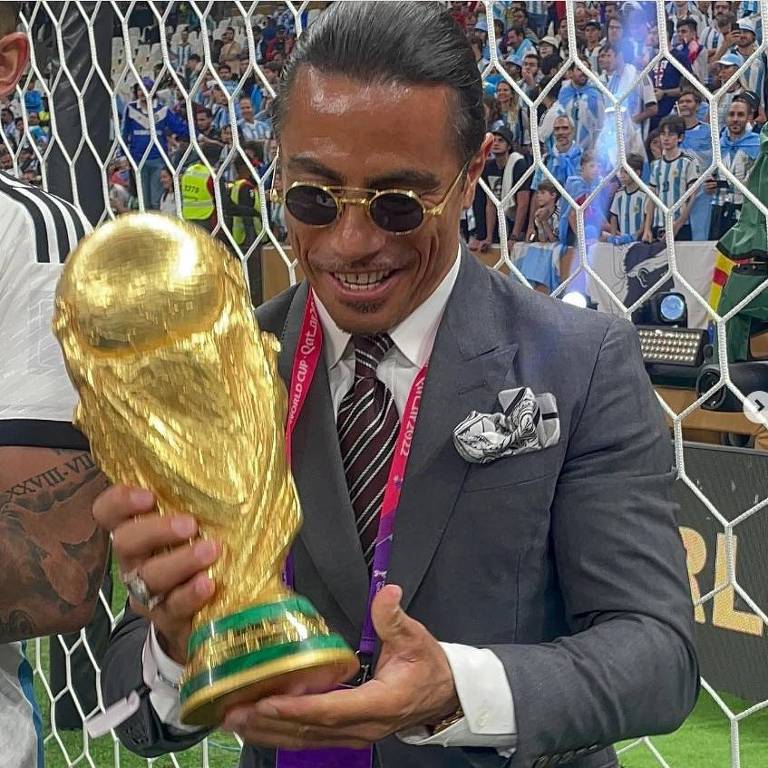 Salt Bae, nome artístico do turco Nusret Gökçe, que ficou conhecido no Qatar por fazer churrasco de R$ 9 mil com tiras de ouro, posa com o troféu da Copa do Mundo no gramado do estádio Lusail