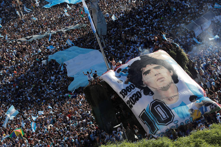 Imagem aérea mostra aglomeração da torcida Argentina durante comemoração, após a conquista do título de campeão mundial, nas ruas da capital Buenos Aires. Uma bandeira com a imagem do Maradona e vista próxima a bandeira nacional. 