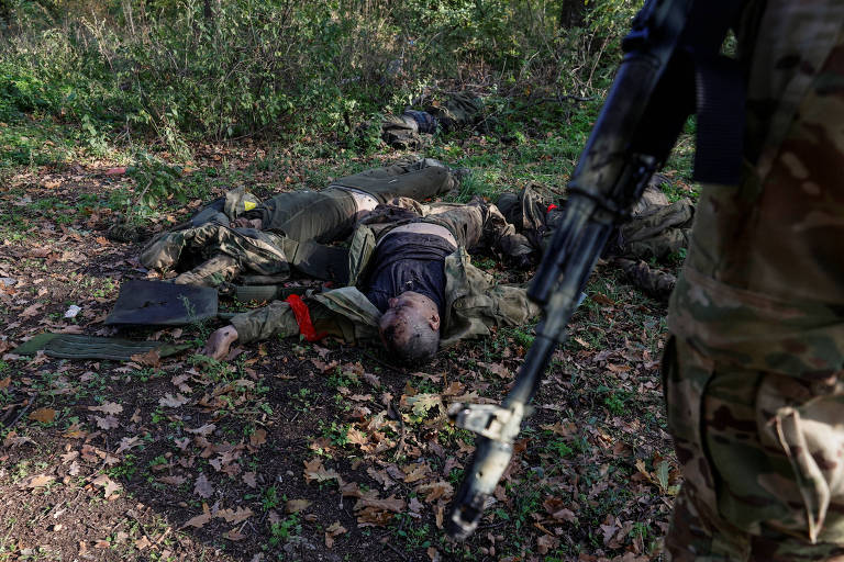 Um oficial ucraniano observa os corpos de soldados russos mortos na Ucrânia, na região de Donetsk, em 7 de outubro de 2022. 
