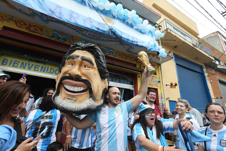 Torcedores comemoram vitória da Argentina pelas ruas da Mooca, zona leste de São Paulo; eles vestem camisa da seleção argentina e carregam cabeça gigante do jogador Diego Maradona. 