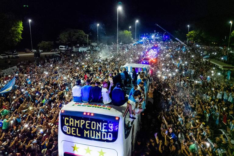 Milhares de torcedores argentinos cercam ônibus em que os campeões mundiais desfilaram de madrugada depois de chegarem do Qatar; no ônibus há a inscrição "campeones del mundo"