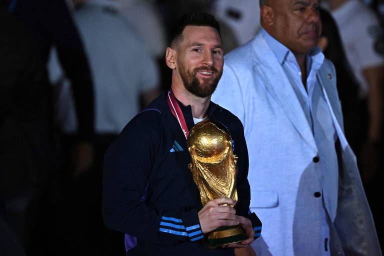 O capitão Messi segura com a mão direita a Taça Fifa e sorri ao desembarcar na madrugada no aeroporto de Ezeiza, na Argentina