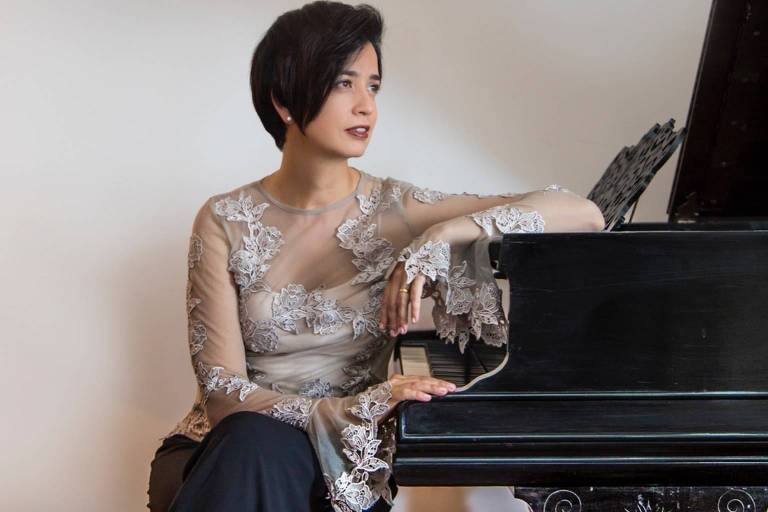 Em foto colorida, a pianista Priscila Bomfim posa para a câmera ao lado do piano
