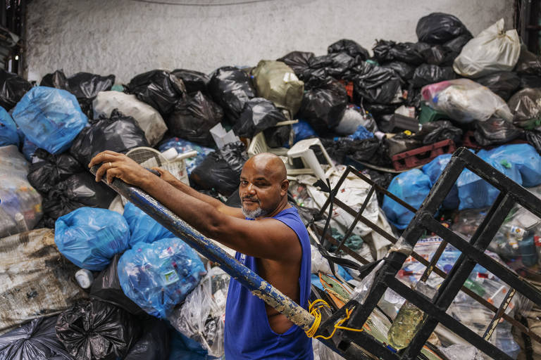 Homem negro e calvo com uma carroça diante de material reciclável acumulado