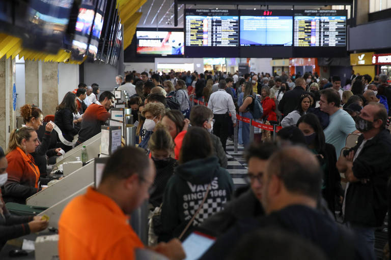 foto mostra aglomeração de passageiros no aeroporto de Congonhas. Ao fundo, é possível ver, fora de foco, painéis de informação sobre horário de voos. 