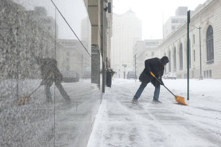 Homem usa pá para tentar remover neve da calçada no centro de Detroit, Michigan, em 23 de dezembro, após tempestade de inverno atingir vários estados nos Estados Unidos. 