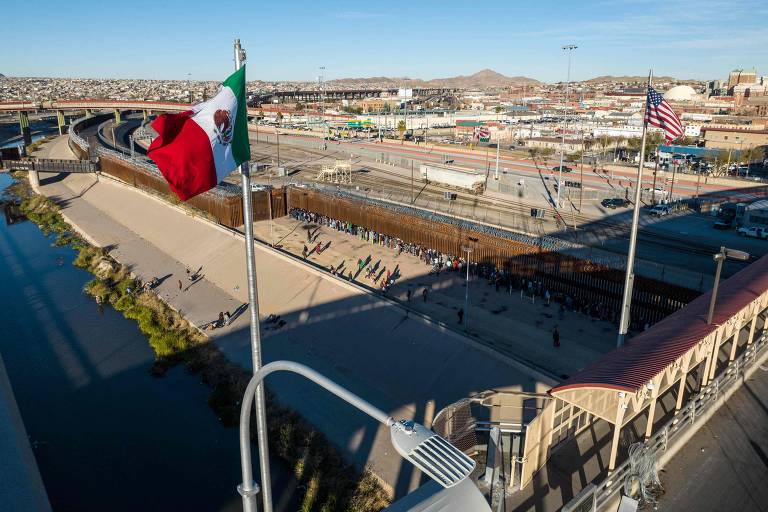 Vista aérea mostra as bandeiras do México e dos Estados Unidos tremulando acima de ponte enquanto migrantes fazem fila junto à cerca entre EUA e México para pedir refúgio, em El Paso, no Texas, em 22 de dezembro.  