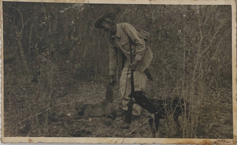 Homem, ao lado de cachorro, arrasta animal caçado