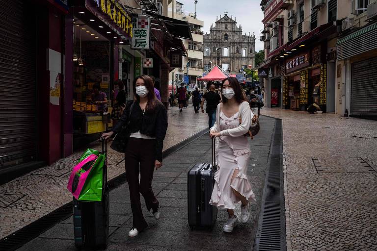 Duas turistas mulheres andam com malas por uma rua, que fica no centro histórico de Macau