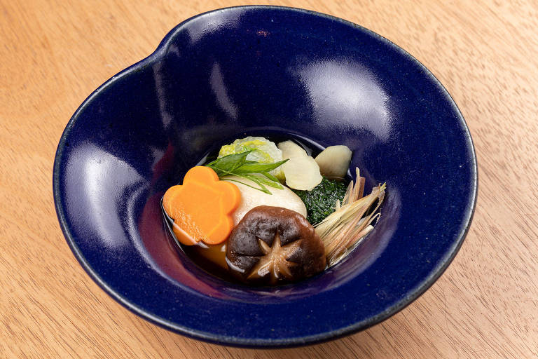 A foto mostra uma tigela azul com uma sopa com legumes como cenoura, cogumelo, bardana e cebolinha