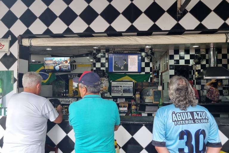 Pessoas acompanham o noticiário da morte de Pelé na Panificadora A Santista, no canal 5 de Santos