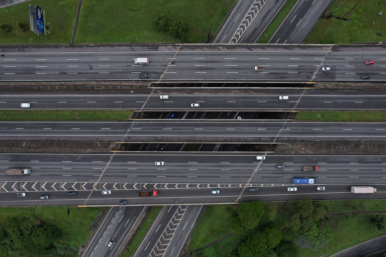 Foto aérea de um viaduto sobre uma outra rodovia. Há carros e caminhões passando.