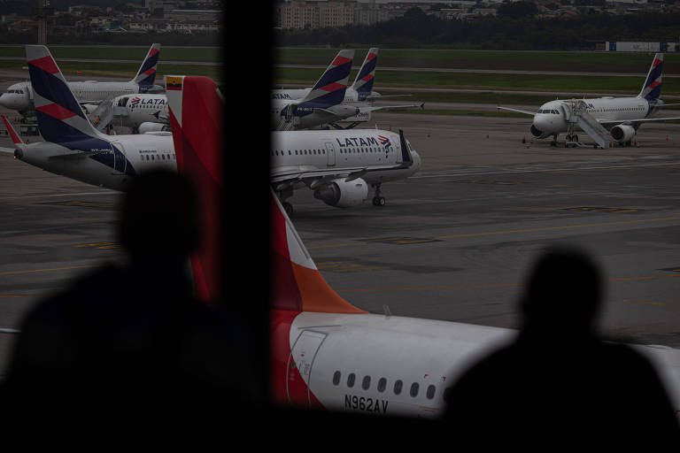 Silhuetas de passageiros observam a movimentação de aeronaves na pista do Aeroporto Internacional de Guarulhos