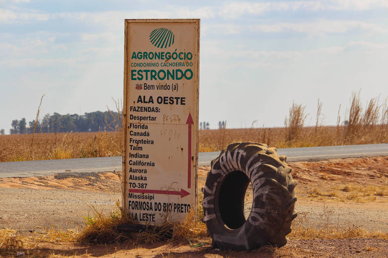 Placa com indicações de fazendas do Estrondo ao lado de uma estrada; ao lado da placa há um pneu antigo de trator