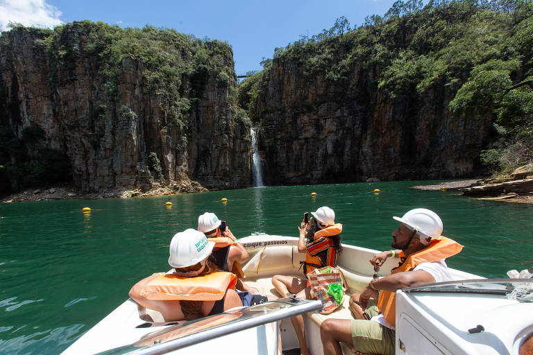 Imagem mostra turistas com coletes salva-vidas e capacetes no lago de Furnas, com cachoeira ao fundo