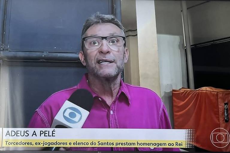 Em foto colorida, homem de camisa rosa dá entrevista para telejornal