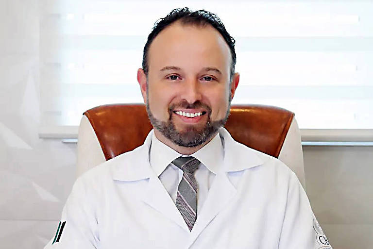 Imagem colorida mostra homem branco sorrindo com jaleco de médico.