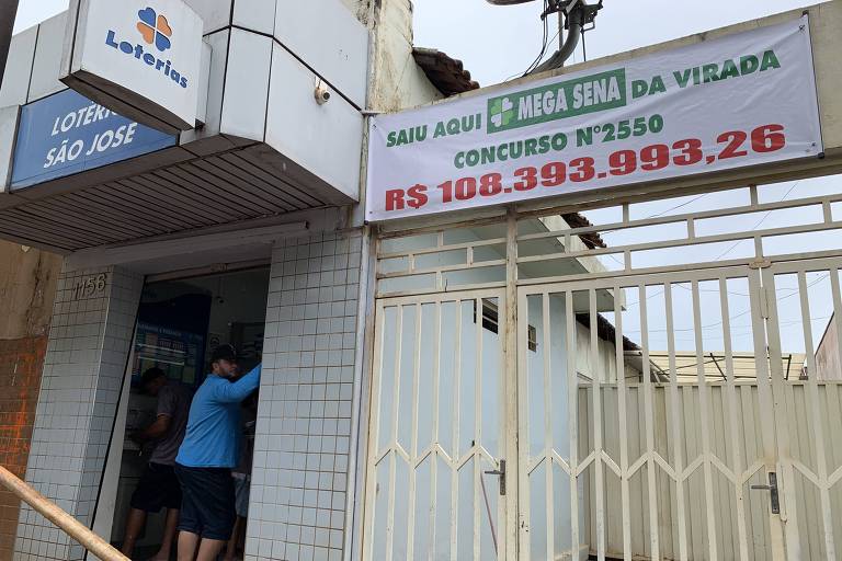 Faixa anuncia que lotérica vendeu bilhete premiado na Mega-Sena da Virada. Na entrada do estabelecimento, está escolado um homem de camiseta azul e boné preto.