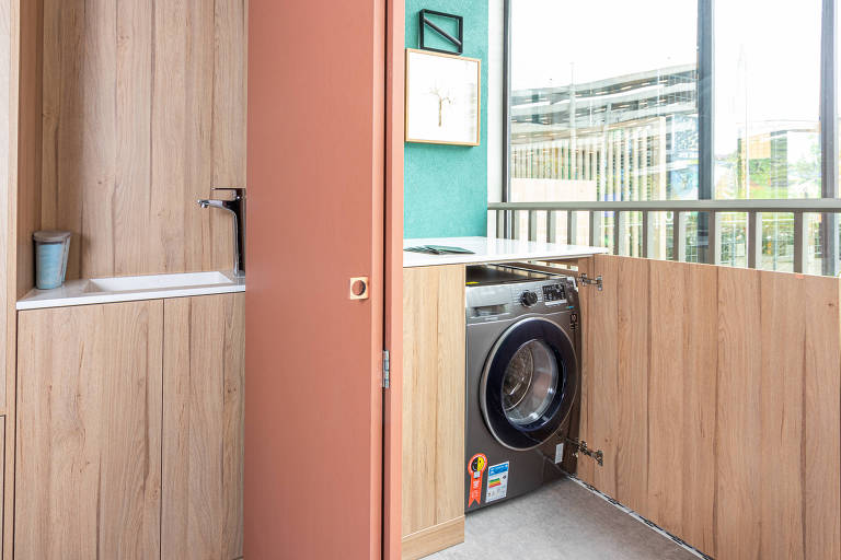 Portas de armário abertas revelam máquina de lavar e tanque escondidos