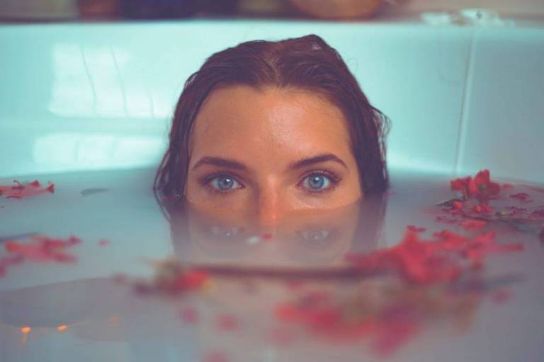 Mulher com cabeça mergulhada em banho de rosas