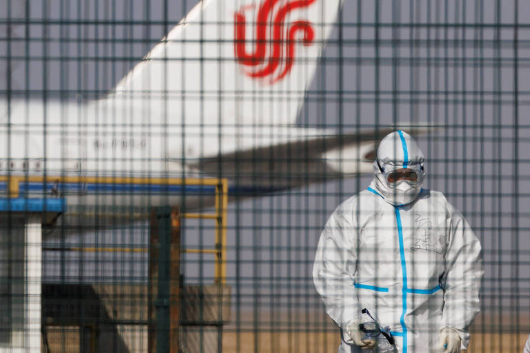 Funcionário com traje de proteção próximo a aeronave no aeroporto internacional de Pequim