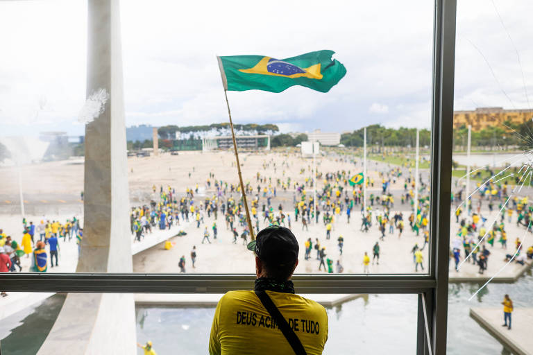 Um homem agita a bandeira do Brasil enquanto apoiadores do ex-presidente Jair Bolsonaro durante invasão do Congresso Nacional em Brasília

