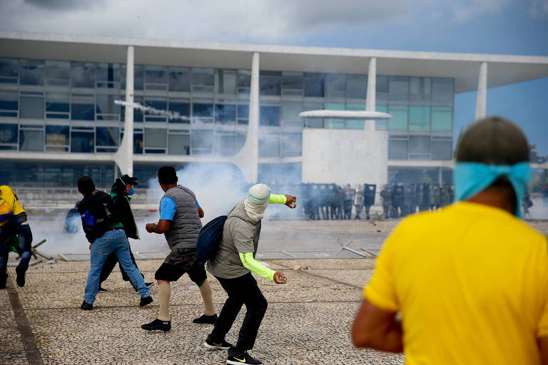 Homens de costas jogam objetos contra policiais em frente ao Palácio do Planalto
