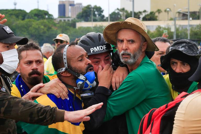 Supporters of Brazilian former President Jair Bolsonaro assist a Military Manifestantes ajudam um policial militar durante confronto