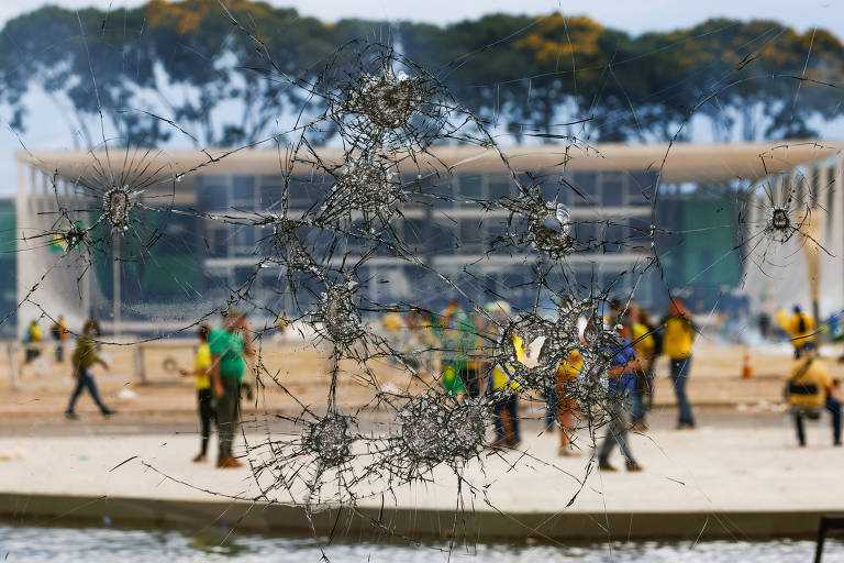 Manifestantes vistos através de um vidro quebrado