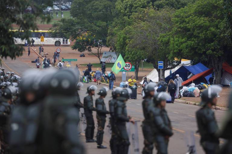 Policiais enfileirados diante de calçada com tendas e bandeira do Brasil