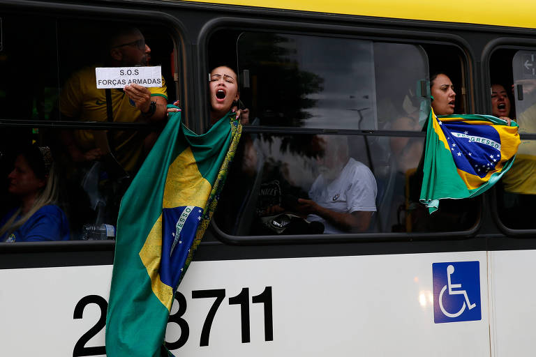 Pessoas gritam e exibem bandeiras do Brasil das janelas de um ônibus; uma pessoa mostra um pedaço de papel em que está escrito "SOS Forças Armadas"