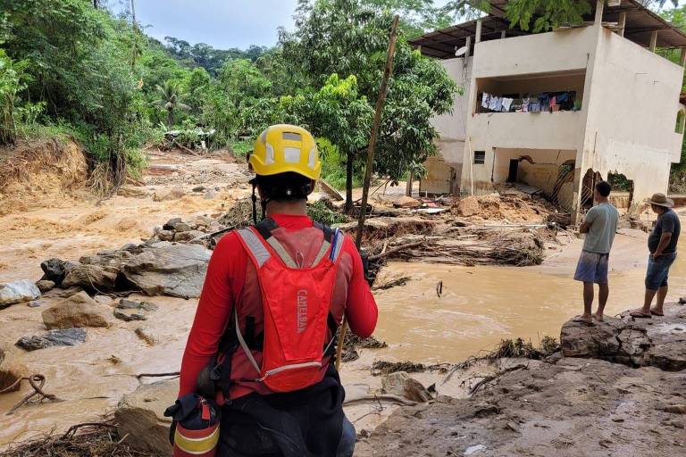 Um bombeiro observa região às margens de córrego em Antônio Dias (MG), onde um homem está desaparecido depois de ser arrastado por enchente.