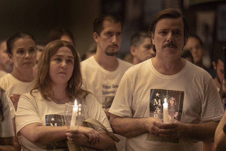 Em foto colorida, uma mulher e um homem aparecem segurando velas nas mãos em um vigília de orações