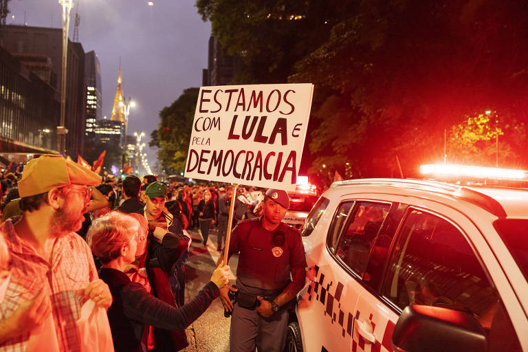 Manifestante segura cartaz em referência ao presidente Lula diante carro da Polícia Militar, durante ato na avenida Paulista