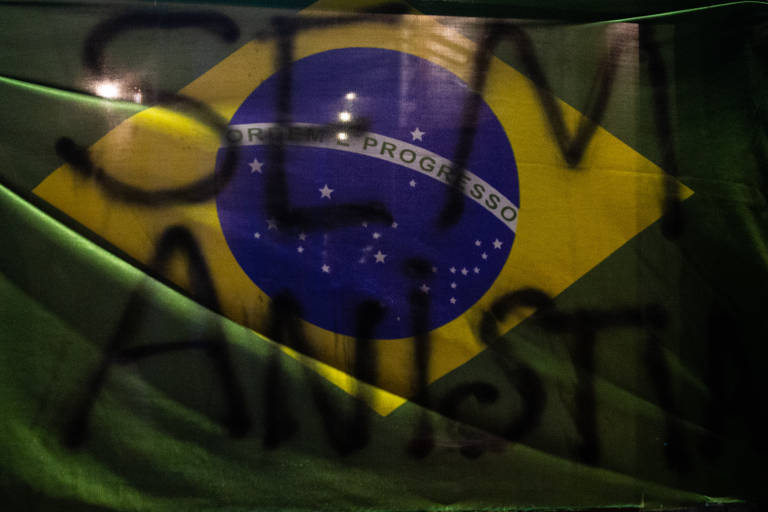 Bandeira do Brasil diante de vidro pichado na avenida Paulista