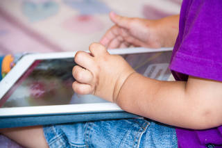 Baby boy is sitting on floor playing with tablet pc. Close-up photo of the hands. Little touch pad, early learning.