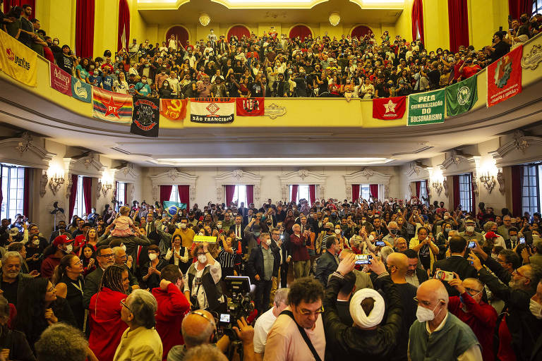 Imagem colorida mostra a visão geral de um teatro lotado, com a plateia e a marquise repletas de pessoas