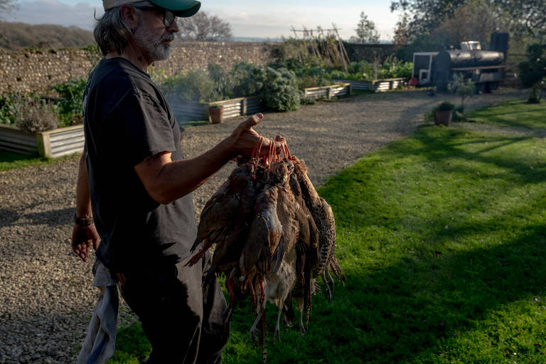 Homem carrega aves mortas para serem preparadas; ele está em um ambiente aberto gramado